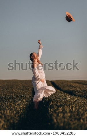 Beautiful young pregnant woman in a dress walks in a summer field at sunset 