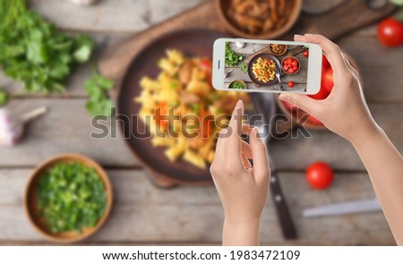 Female food photographer with mobile phone taking picture of tasty pasta with chicken, top view