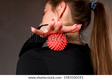 Photo from behind. The girl relaxes the muscles of the back with the help of a massage ball, running it with her hand on the back