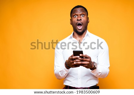 Handsome african american businessman holding a phone in his hands and looking at the camera surprised Royalty-Free Stock Photo #1983500609