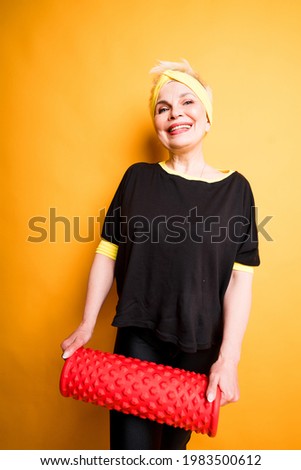 Cute elderly woman in black t-shirt smiles and holds fascia in her hands while looking at the camera