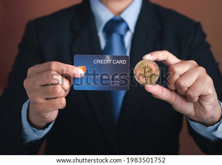 Hand of a businessman holding a bitcoin golden coin and a mockup blue credit card while standing with a brown background. Close-up photo. Virtual cryptocurrency and future money concept.