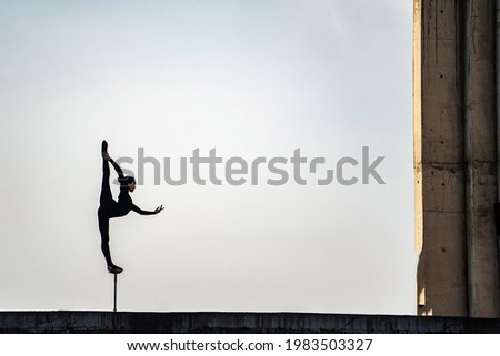 Silhouette of flexible girl keeping balance in split on sky background. Concept of individuality, creativity and outstanding