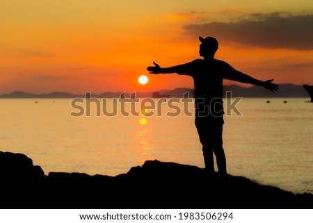 A young boy in a pool enjoying the sunset. Human silhouette over the setting sun. Holding sun in hand. Seascape. Copy space banner. Beautiful sky background. Balance.