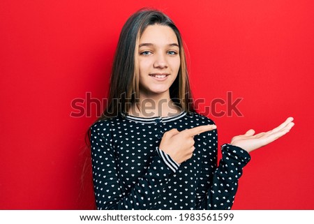 Young brunette girl wearing casual sweater amazed and smiling to the camera while presenting with hand and pointing with finger. 
