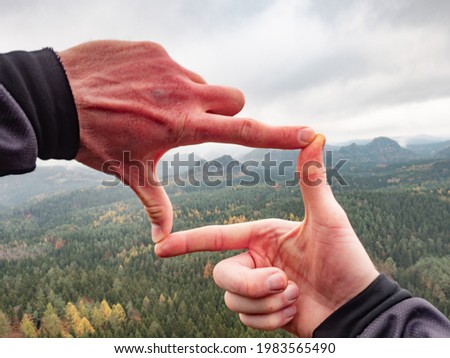 Man looking at hilly landscape framing with fingers, searching for image composition as he hiking over the mountain range. Landscape photographer 