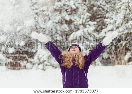 Girl in snowy hat throwing snow outdoors winter trees background
