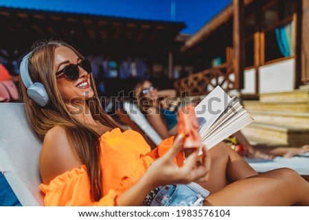 Young beautiful girl smiling reading a book at the swimming pool stock photo. Summer vacation with a great book. Woman reading near the pool.