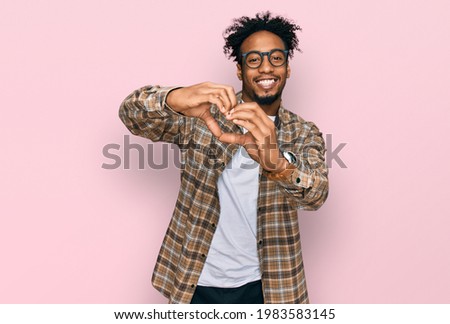 Young african american man with beard wearing casual clothes and glasses smiling in love doing heart symbol shape with hands. romantic concept. 