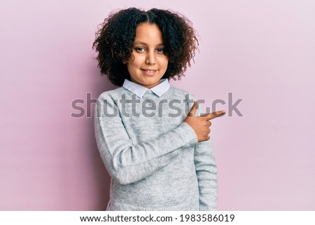 Young little girl with afro hair wearing casual clothes smiling cheerful pointing with hand and finger up to the side 