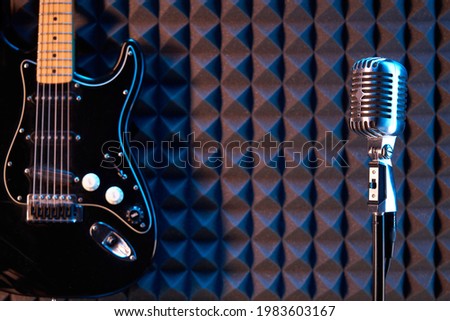 Studio condenser microphone and black electric guitar, on acoustic foam panel background