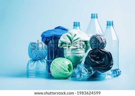 Plastic recycling and reuse concept. Empty plastic bottle and various fabrics made of recycled polyester fiber synthetic fabric on a blue background. Environmental protection waste recycling. Royalty-Free Stock Photo #1983624599