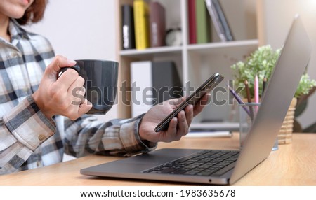 Young Businesswoman holding coffee cup and using smartphone for sms messages technology and Social media network concept.