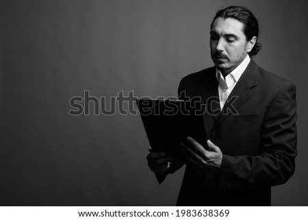 Studio shot of handsome businessman with mustache wearing suit against gray background in black and white