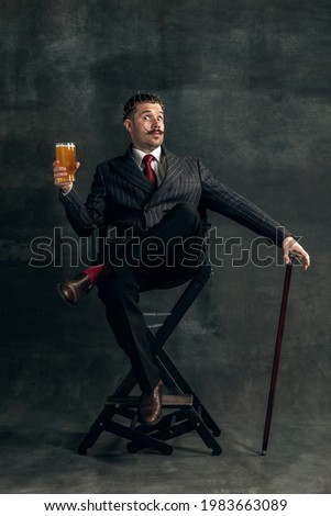 Fashion king. Young man with glass of beer in art action remaking greatest artist Salvador Dali and its pictures isolated on vintage background. Retro style, comparison of eras, fashionable characters