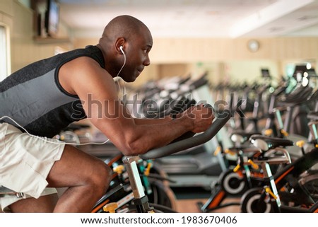 Athletic black man doing cardio workout on exercise bike in gym. Concept of sport and healthy lifestyle. Royalty-Free Stock Photo #1983670406