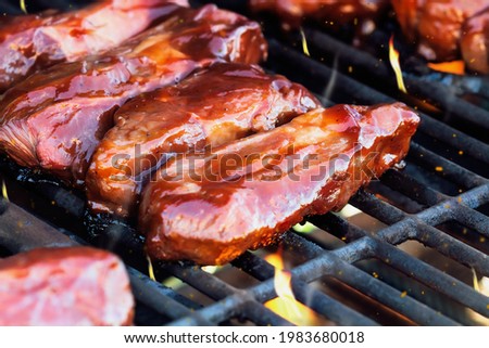 Boneless beef ribs grilling over flames with tangy barbecue sauce for a summer cook out. Extreme shallow depth of field with blurred background and foreground.