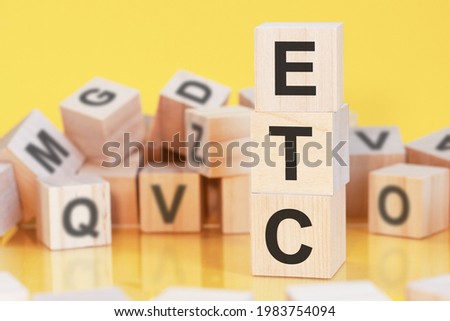 wooden cubes with letters ETC arranged in a vertical pyramid, yellow background, reflection from the surface of the table, business concept. etc - short for electronic trade confirmation Royalty-Free Stock Photo #1983754094