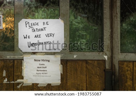 Rustic sign in restaurant window during time of Covid stating restaurant is understaffed and is hiring in a struggling economy, showing the plight of small businesses in the post-pandemic economy. Royalty-Free Stock Photo #1983755087
