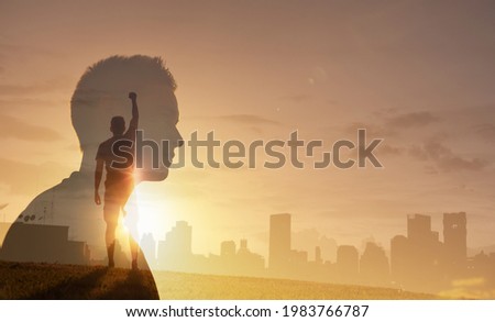 Modern day supper hero. Young confident man stands at rooftop with fist pump facing cityscape view and thinking. People power, feeling motivated looking to the future.