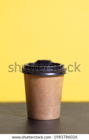 Disposable coffee cup for a cafe on a yellow background. Brown cardboard mockup of an eco-friendly coffee cup in a vertical photo. Disposable Plastic and Paper Hot Drinks Template