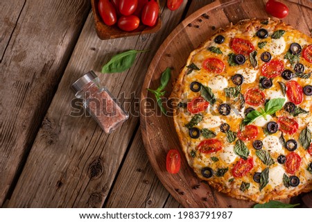 In the right corner of the photo we see a pizza on a wooden stand. To the left of the pizza are spices in a glass bottle, and in the background we see tomatoes. Wooden table. Country style.