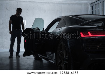 Successful Caucasian Men in His 40s Looking at His Luxury Exotic Car Inside Underground Garage. Car Enthusiast Collection. Royalty-Free Stock Photo #1983816185