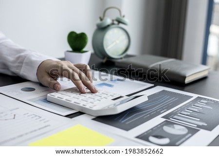 A businesswoman is pressing a white calculator to calculate the financial figures on the company's quarterly financial summary, prepared from the Finance Department. Company financial concept.