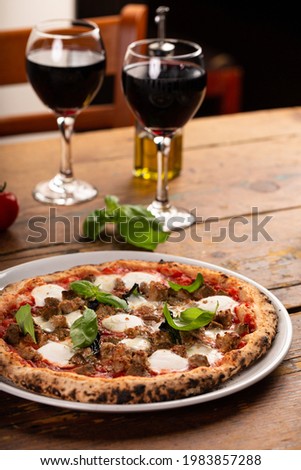 Freshly baked Neapolitan pizza with mozzarella and fresh basil on a wooden table served with wine