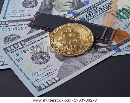 yellow bitcoin, an m2 SSD disk and hundred-dollar bills lie on a black background. The concept of mining cryptocurrency through hard drives. Side view
