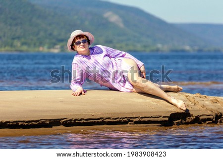 beautiful mature woman lies on a small sandy island in the middle of the Volga river