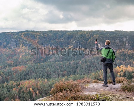 Man takes smart phone mobile photo on mountain landscape. Autumn season hike