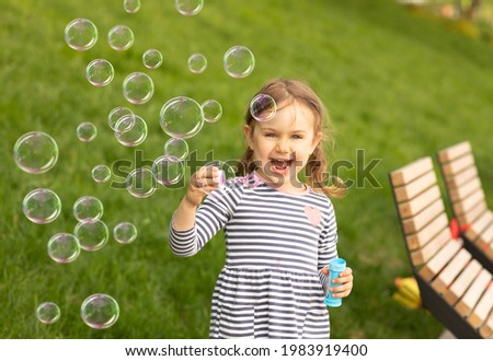 Smiling emotional laughing expression child girl blowing soup bubbles in summer nature. Fresh green grass background.Soap bubbles flying.Outdoors activities, summer holidays with kids.