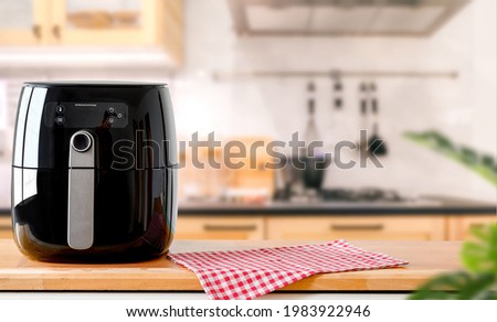 An electric Air Fryer on table with blurred kitchen background.  Lifestyle of new normal cooking.  Royalty-Free Stock Photo #1983922946