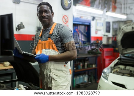 American auto mechanic diagnosing car engine with a laptop at the car repair service center