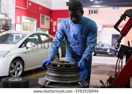 Afro american man working with tire fitting machine at auto car repair service center