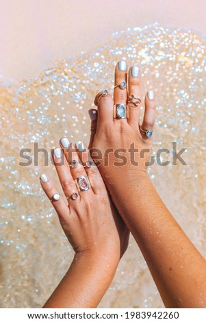 beautiful young woman hand with many rings at sea shore background close up 