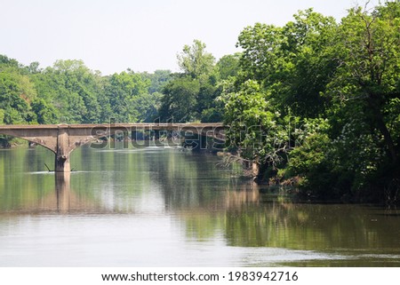 old abandoned concrete arch roadway or train railway bridge over a calm river with trees and clear sky
