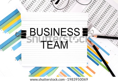 Notebook with pencils, glasses on graph background, with text BUSINESS TEAM