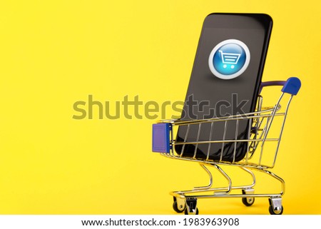Online shopping, phone and shopping cart concept, for sale at a discount on a yellow background.   Delivery. Copy space. 