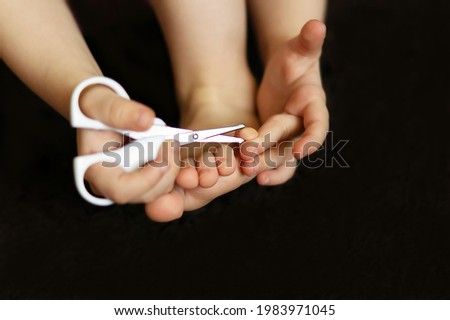 A small child cuts her nails with a safe pair of scissors in close-up. A charming girl cuts her toenails with a pair of nail scissors. Healthy hygiene procedures, baby nail care concept