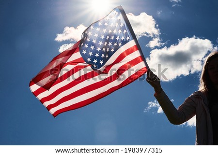 American flag outdoors. Woman silhouette holds usa national flag against blue cloudy sky. 4th July Independence Day