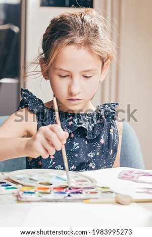 Cute girl draws with paints. Ideas for activities with children at home. Vertical shot