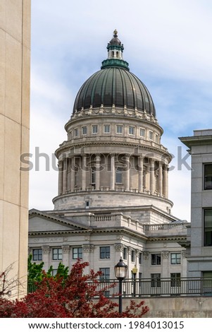 Famous landmark Utah State Capital Building against cloudy sky in Salt Lake City. Building exterior, trees and street light can be seen in the foreground.
