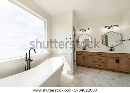 Luxurious bathroom interior with hexagon cut tile flooring and large picture window with sky view. Freestanding tub with floor mount faucet with hand shower beside shower stall near the vanity sink.