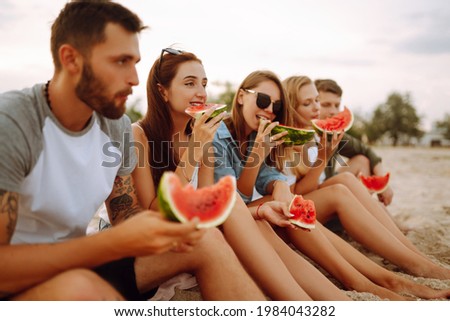 Young friends relaxing on the beach and eating watermelon. Group of people enjoy summer party together. People, lifestyle, travel, nature and vacations concept.