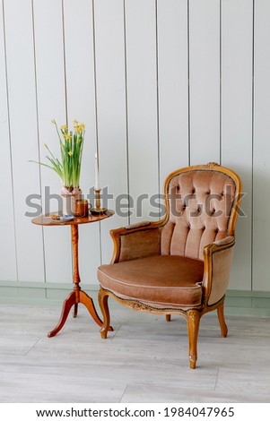 Stylish vintage chair with patterns of wood aristocratic type Brown chair Yellow flowers in pot and candles with a mug on a wooden table On floor purple dried flowers in wicker basket Green background