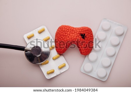 Treatment of diseases of thyroid concept. Model of thyroid and pills on a pink background