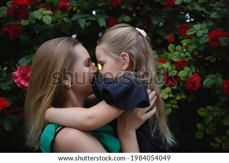 family portrait. mom hugs and kisses her little daughter against the background of a rose bush.