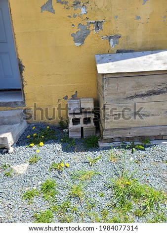 Six cement bricks or cinder blocks piled neatly on top of each other in a crisscrossing pattern. They're piled in a yard filed with gravel gravel, next to a short stoop, and a cedar chest.